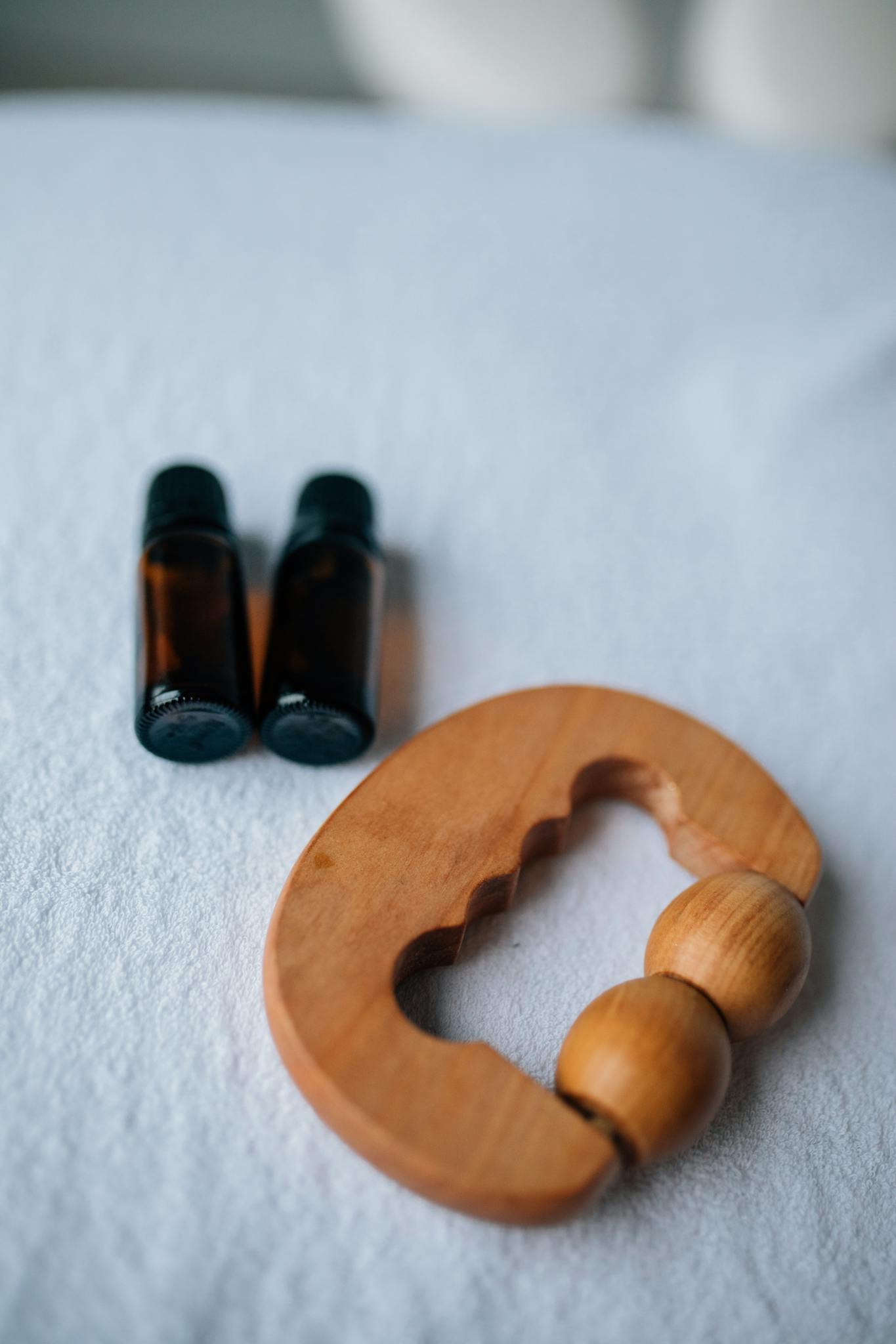 Close-up of essential oil bottles and a wooden massager on a soft surface.