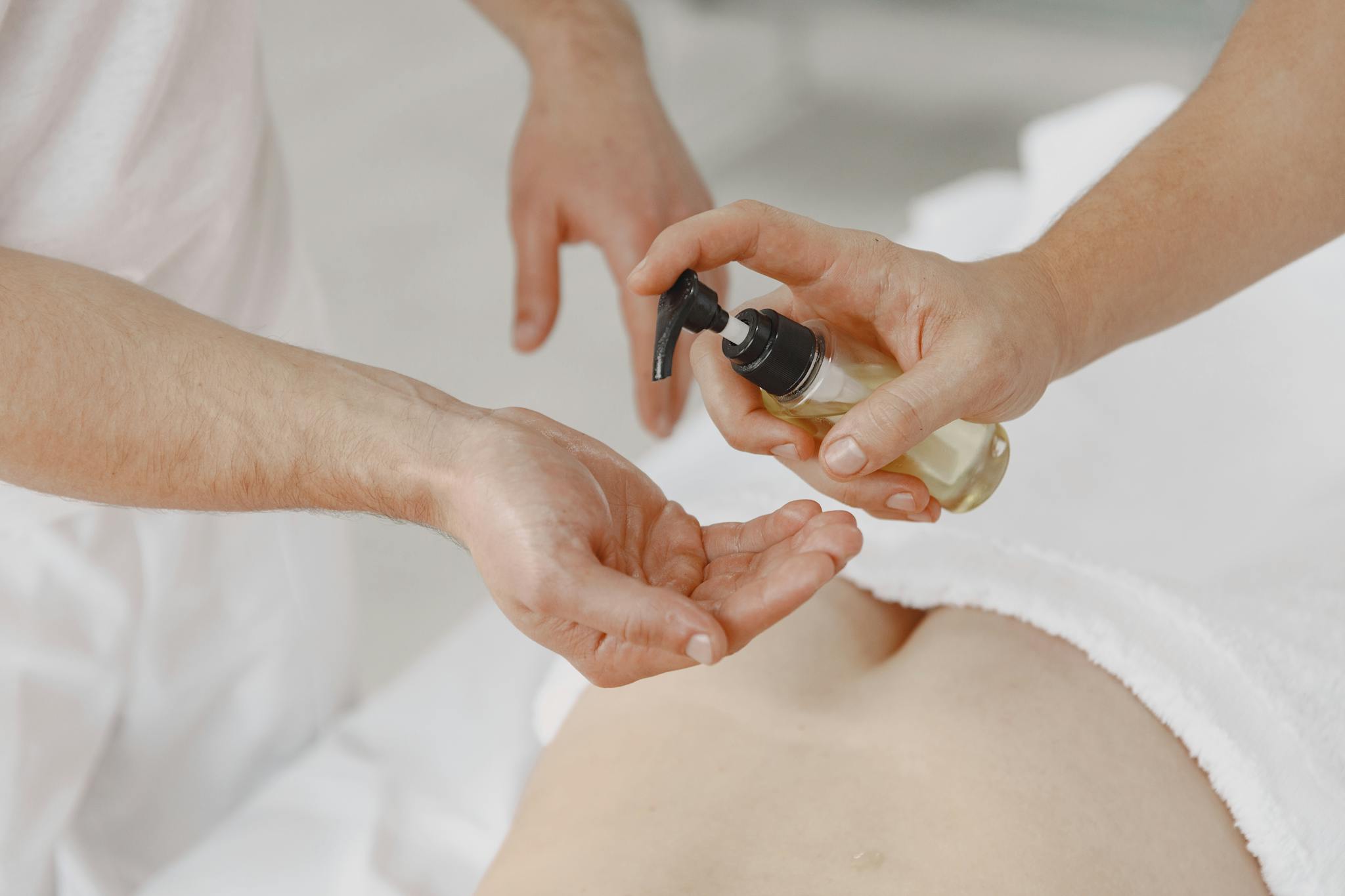 Close-up of hands using a pump bottle during a massage session, applying essential oils for relaxation.
